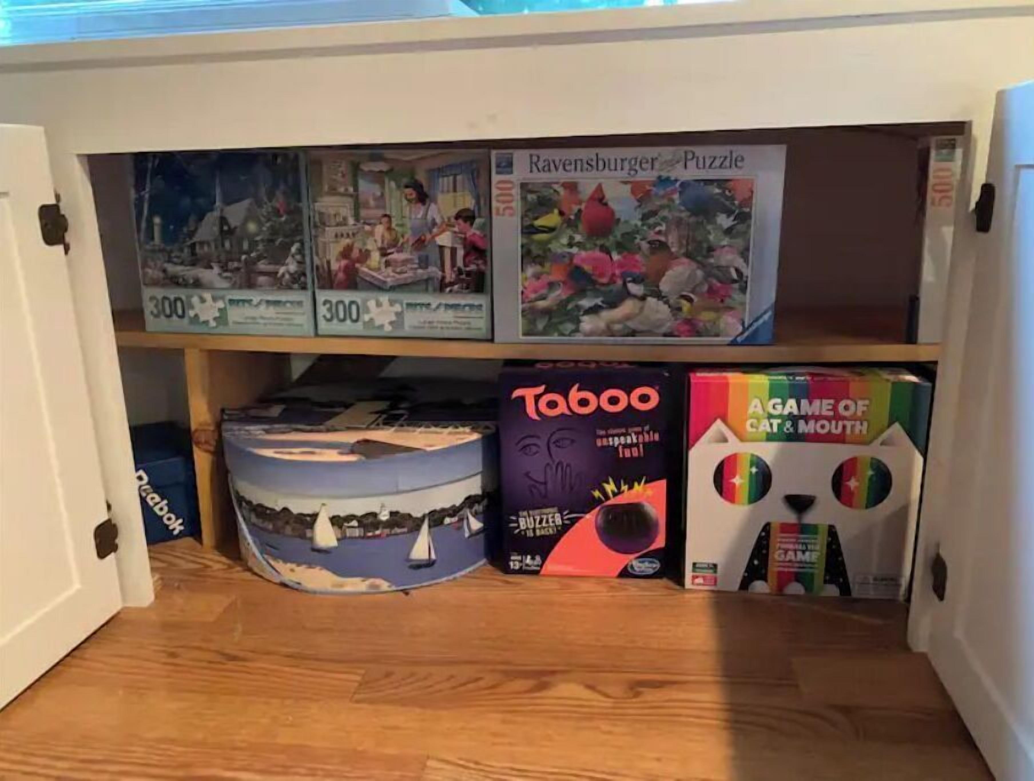 Uma estante com diversos jogos de tabuleiro, incluindo 'Ravensburger Puzzle', 'Taboo' e 'Game of Cat & Mouth'.