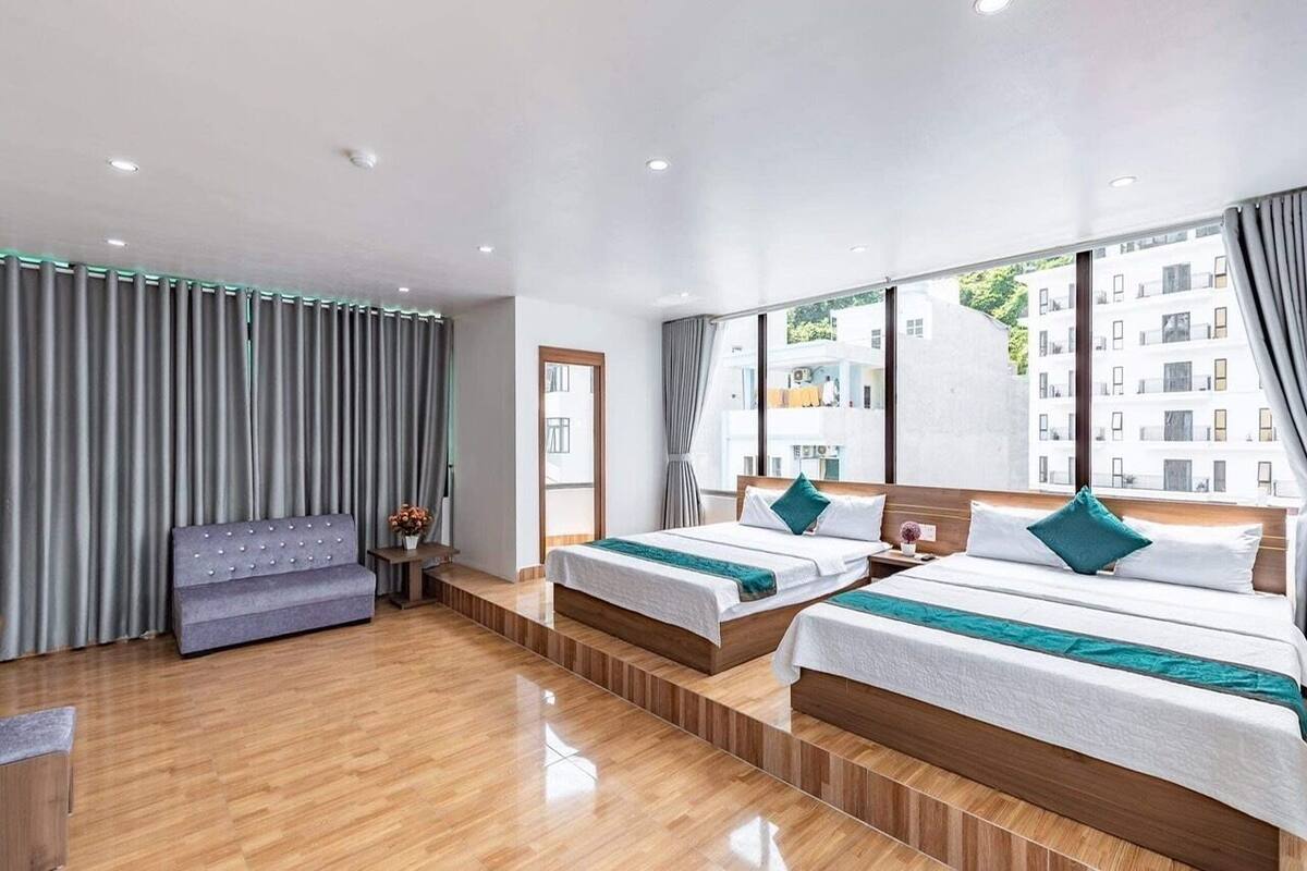Una habitación de hotel moderna con dos camas, un sofá y vistas a edificios a través de amplios ventanales.