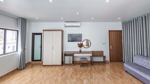 Ein modernes Hotelzimmer mit Holzboden, Schreibtisch und Stuhl, einer Couch, einem an der Wand montierten Fernseher und einem Kleiderschrank.