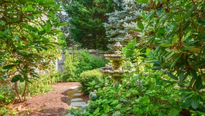 Ein Garten mit einem Steinkrug, einem Kiesweg und verschiedenen Pflanzen.
