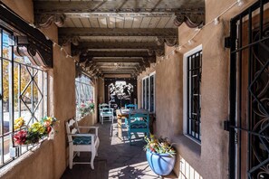 A covered outdoor seating area with wooden tables and chairs, potted plants, and a view of the street. - Turquoise Butterfly by Kokopelli Property Management (Santa Fe)