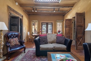 A cozy living room with a leather armchair, a sofa, and a coffee table. There is a patterned rug on the floor, and the room has wooden doors and a ceiling with exposed beams. - Turquoise Butterfly by Kokopelli Property Management (Santa Fe)