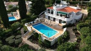 En stor, hvid villa med swimmingpool, omgivet af frodig vegetation og palmer.