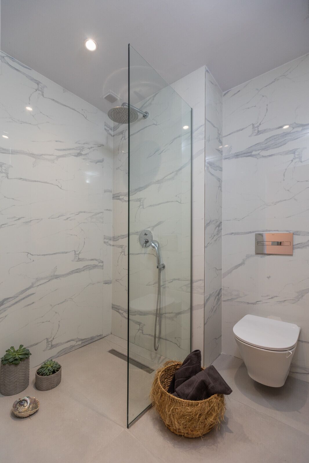 Een moderne badkamer met een douchecabine van glas, een toilet en een klein rieten mandje met handdoeken.