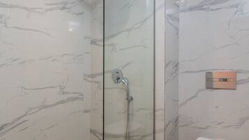 Een moderne badkamer met een douchecabine van glas, een toilet en een klein rieten mandje met handdoeken.
