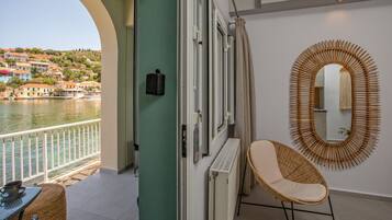 Un balcon donnant sur un plan d’eau et des bâtiments, une chaise en osier, un radiateur et un miroir fixé au mur.