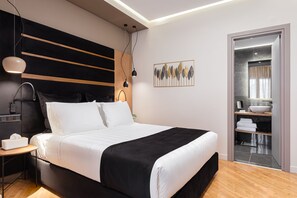A modern bedroom with a large bed, bedside tables, a nightstand, a wall-mounted lamp, and a bathroom visible through an open door.