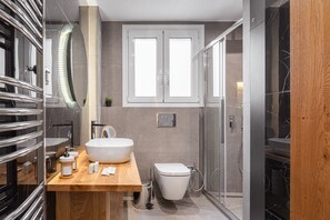 A modern bathroom with a wooden vanity, a large white sink, a toilet, and a glass shower enclosure.