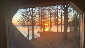 A view through a window of a lakeside property with a wooden deck and a clear sky. - Lake house, amazing view, hot tub (Perryville)