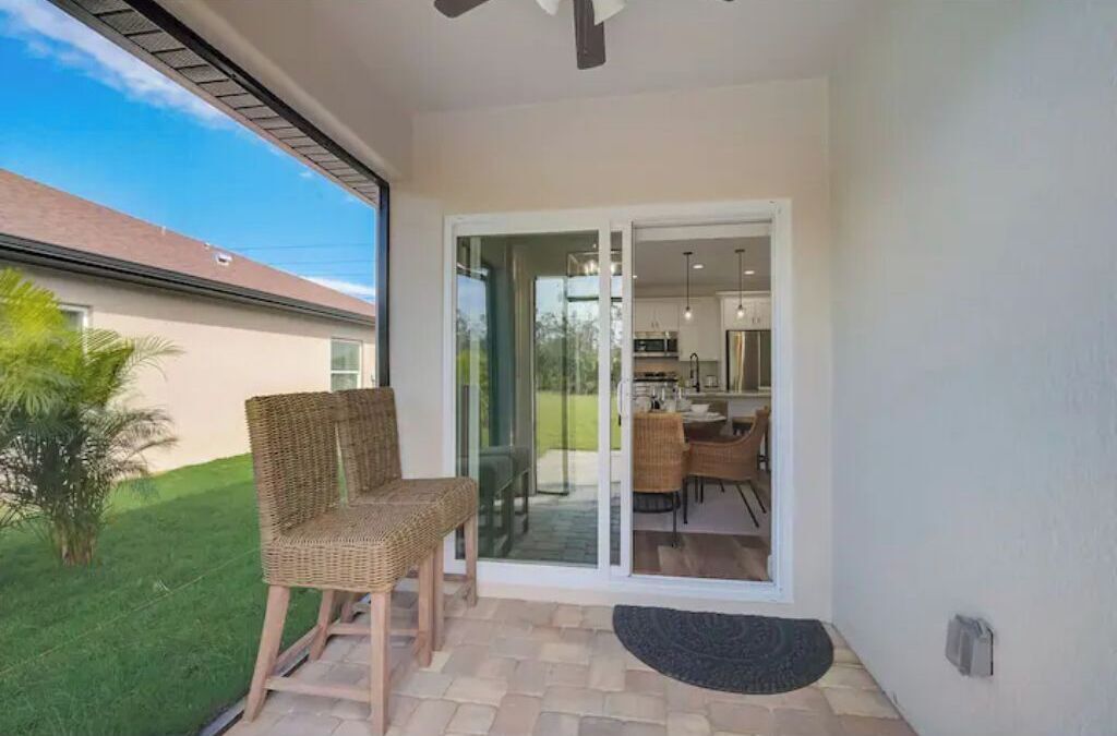 Ein Balkon mit Korbstühlen, einem kleinen Teppich und Blick auf ein Haus und einen Garten.