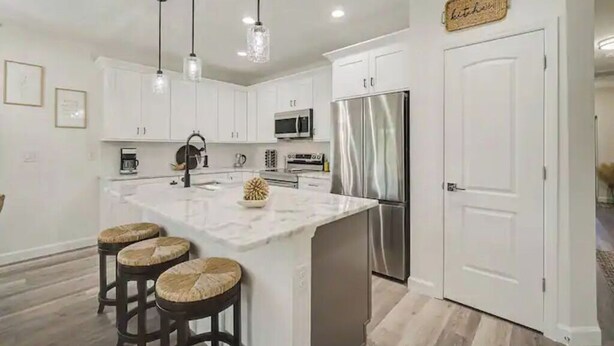 A modern kitchen with white cabinets, a stainless steel refrigerator, and a central island with stools.