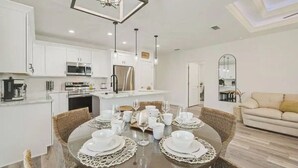 A modern kitchen with white cabinets, stainless steel appliances, and a dining area set for six with a round table and wicker chairs.