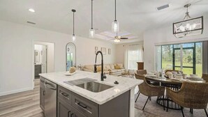 A modern kitchen with a central island, stainless steel appliances, pendant lighting, and a dining area with wicker chairs.