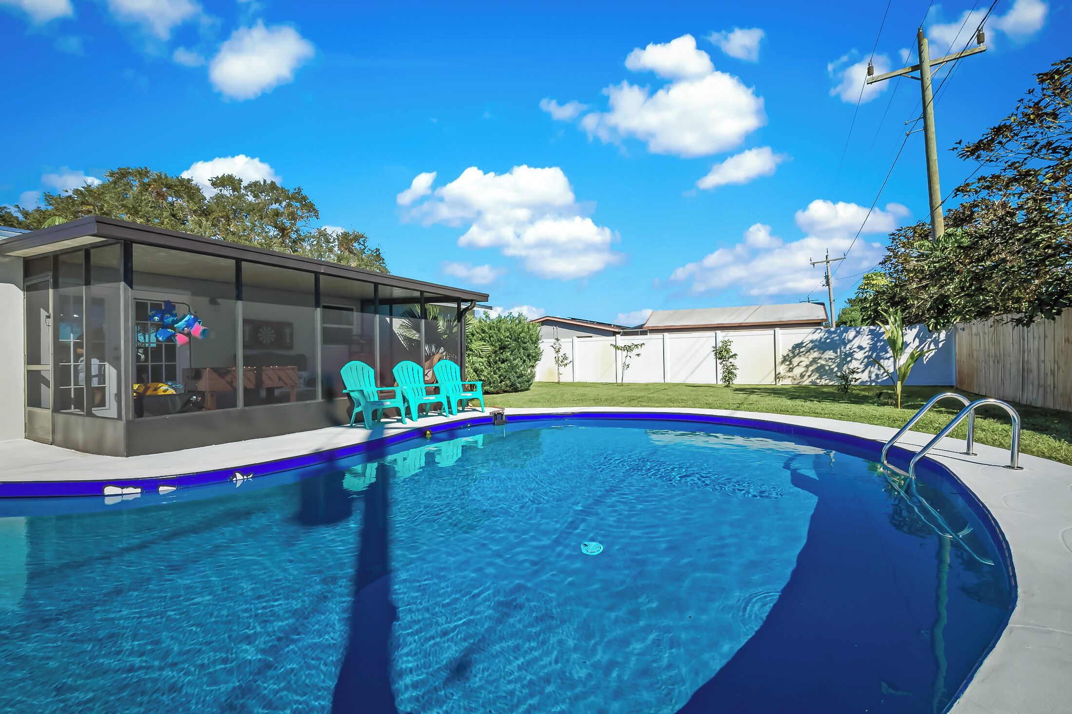 Una piscina con agua cristalina azul, rodeada por una valla de madera y un césped.