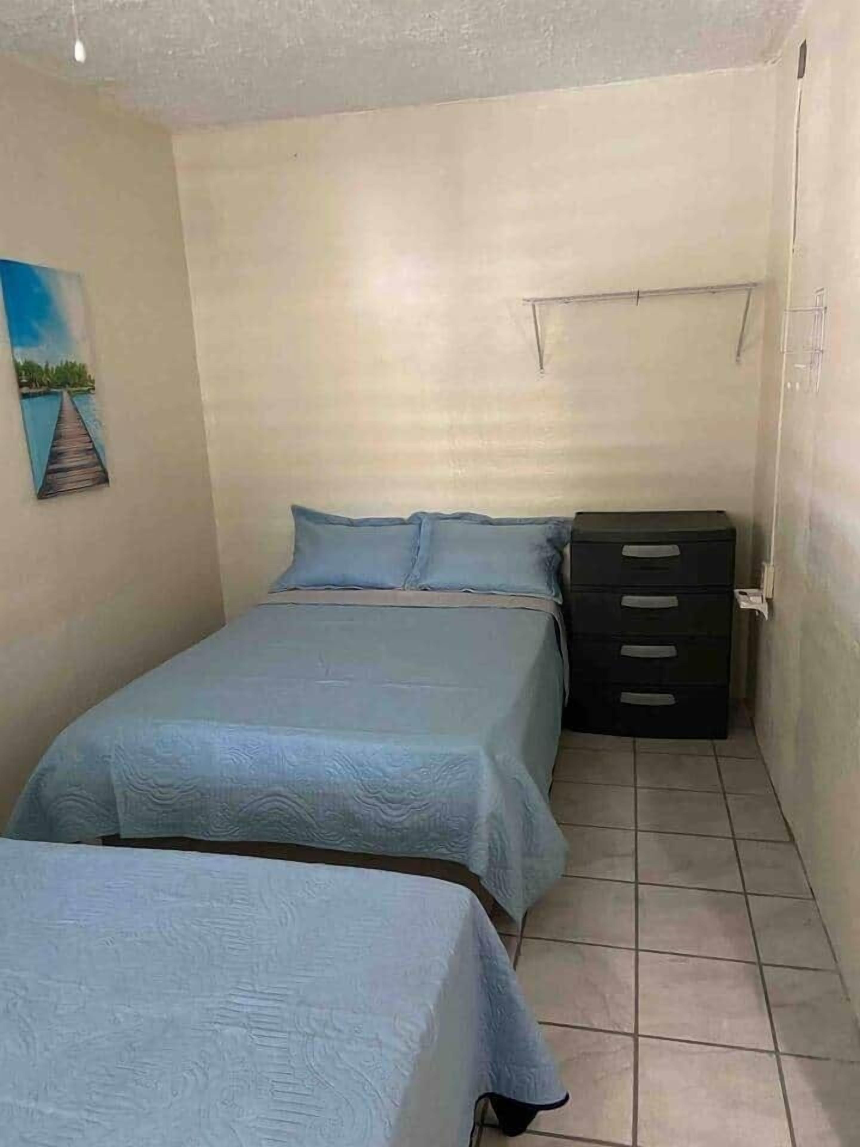 A small, simple room with two beds, a dresser, and a painting on the wall.