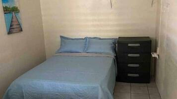 A small, simple room with two beds, a dresser, and a painting on the wall.
