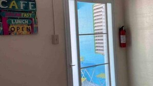 A room with a door leading to an outdoor area, a fire extinguisher mounted on the wall, and a colorful sign on the wall. - Cayo Laurel at Guayacan Guest House (Lajas)
