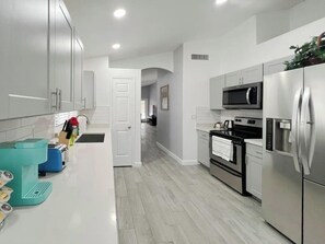 Cocina moderna con armarios blancos, electrodomésticos de acero inoxidable y encimera verde azulado.