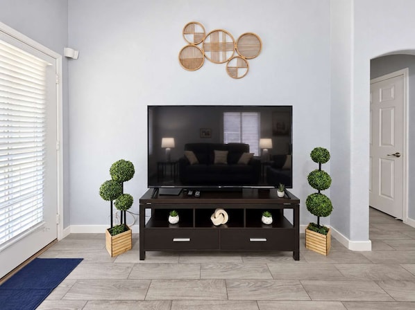 Una sala de estar moderna con televisor de pantalla plana, mueble de madera oscura para entretenimiento, decoración mural y plantas en macetas.