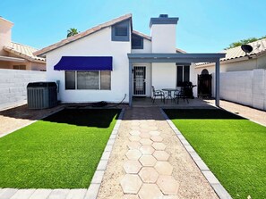 Een gelijkvloers huis met een terras, een overdekte zitplaats buiten en een verzorgd gazon.