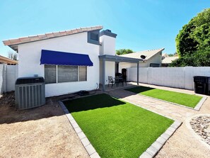 Een modern huis met terras, kunstgras en een overdekte zithoek buiten.
