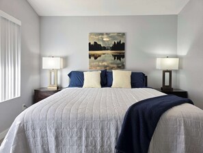 Een slaapkamer met een bed, twee nachtkastjes, een raam met zonwering en een aan de muur hangend schilderij.