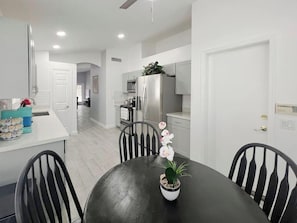 Una cocina moderna con armarios blancos, un refrigerador de acero inoxidable y una zona de comedor con una mesa y sillas negras.