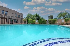 A swimming pool with a tiled edge, surrounded by a fence and a building with a flat facade.