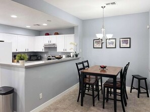 A modern kitchen with white cabinets, a dining table with chairs, and a trash can.