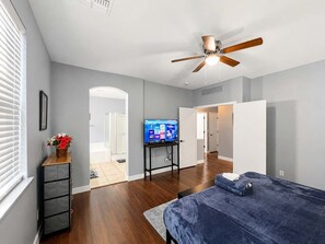 Una camera da letto con un letto, una ventola a soffitto, un televisore e una porta che dà su un'altra stanza.