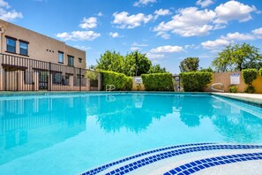 Una piscina con superficie d'acqua cristallina e blu, circondata da una recinzione e da vegetazione.