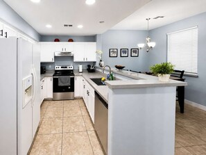 Una cucina moderna con mobili bianchi, un'isola centrale, elettrodomestici in acciaio inossidabile e una parete di colore azzurro chiaro.