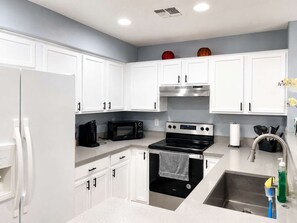 A kitchen with white cabinets, a black microwave, a stainless steel stove, and a sink with a faucet.