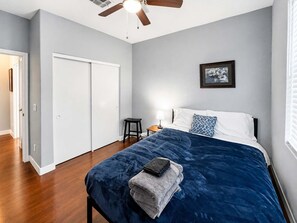 A bedroom with a bed, a nightstand, a ceiling fan, and a door.
