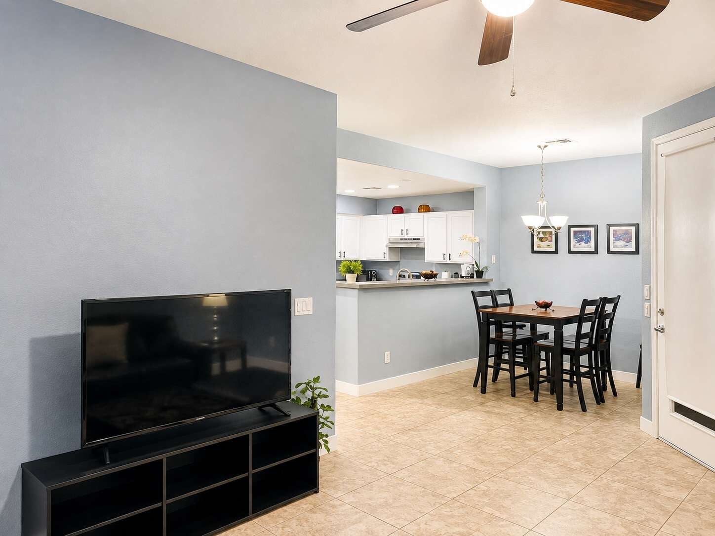 A living room with a flat-screen TV, a dining area with a table and chairs, and a kitchen in the background.