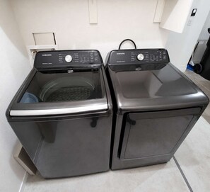 A pair of Samsung washing machines in a room with a tiled floor and white walls.