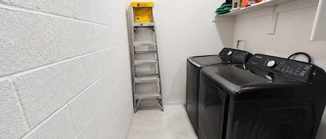 A laundry room with a washing machine, a drying rack, and shelves with cleaning supplies.