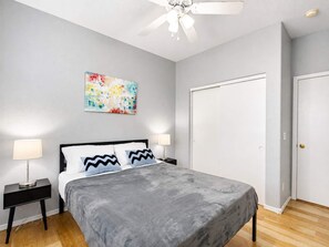 A bedroom with a bed, two bedside tables, a ceiling fan, a door, and a wall-mounted artwork. - Pet-Friendly 3BR | Community Pool | Near ASU (Tempe)