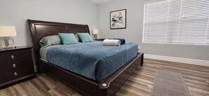 A bedroom with a bed, nightstands, a dresser, a window with blinds, and a wall-mounted artwork. - Chandler Pool Home | King Bed | Pet Friendly (Chandler)