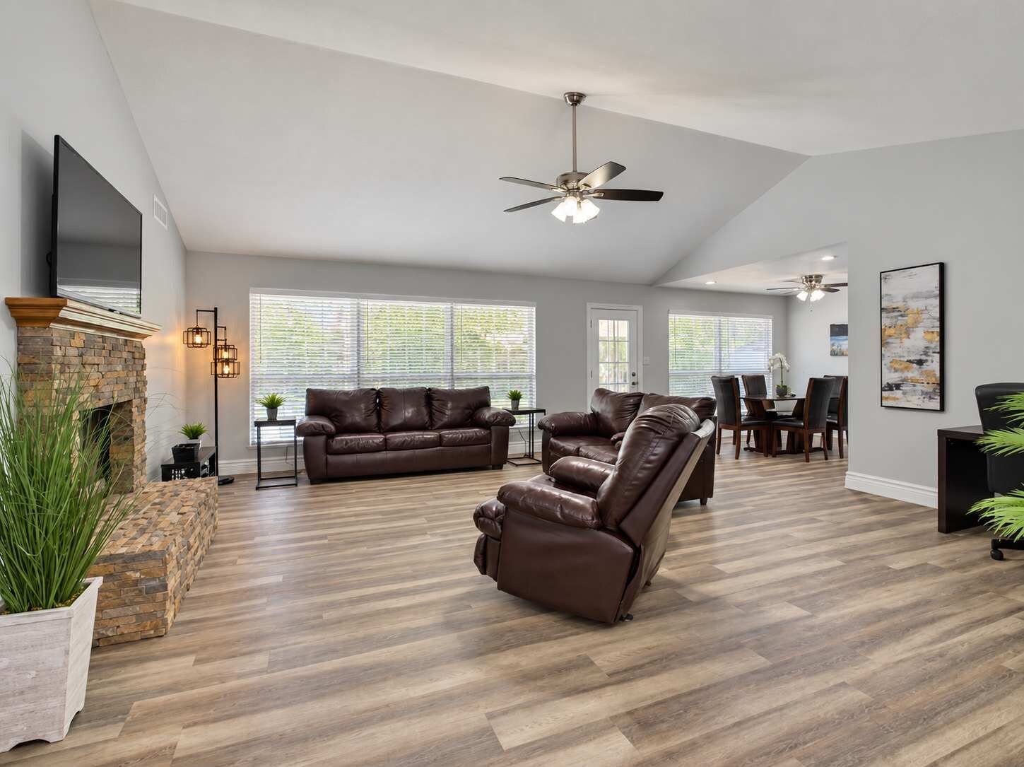 A spacious living room with a fireplace, leather sofas, a dining area, and a ceiling fan.