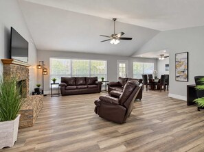 A spacious living room with a fireplace, leather sofas, a dining area, and a ceiling fan. - Chandler Pool Home | King Bed | Pet Friendly (Chandler)