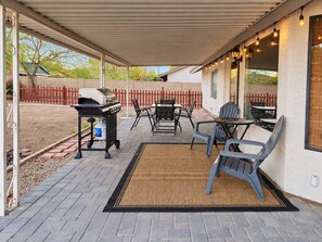 An outdoor patio with a grill, seating, and string lights.