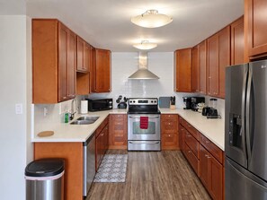 A compact kitchen with wooden cabinets, stainless steel appliances, and a tiled backsplash.