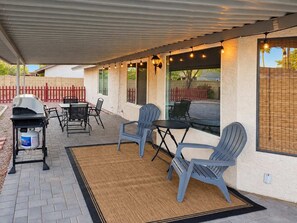 An outdoor patio with a grill, seating, and string lights.