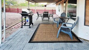 Un patio techado con una parrilla, asientos exteriores y luces colgantes.