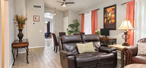 A living room with a leather sofa, a dining area with chairs, a table, and a TV.