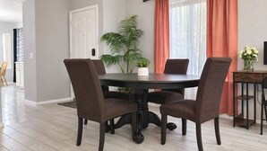 A dining area with a round table, four chairs, a television, and a potted plant.