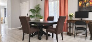 A dining area with a round table, four chairs, a television, and a potted plant.