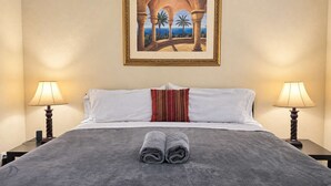 A hotel room with a bed, two bedside lamps, a painting on the wall, and a pair of towels on the bed.