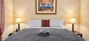 A hotel room with a bed, two bedside lamps, a painting on the wall, and a pair of towels on the bed.